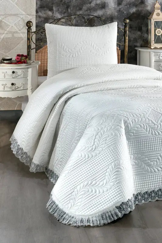 White quilted bedspread with lace trim and geometric pattern detailing.