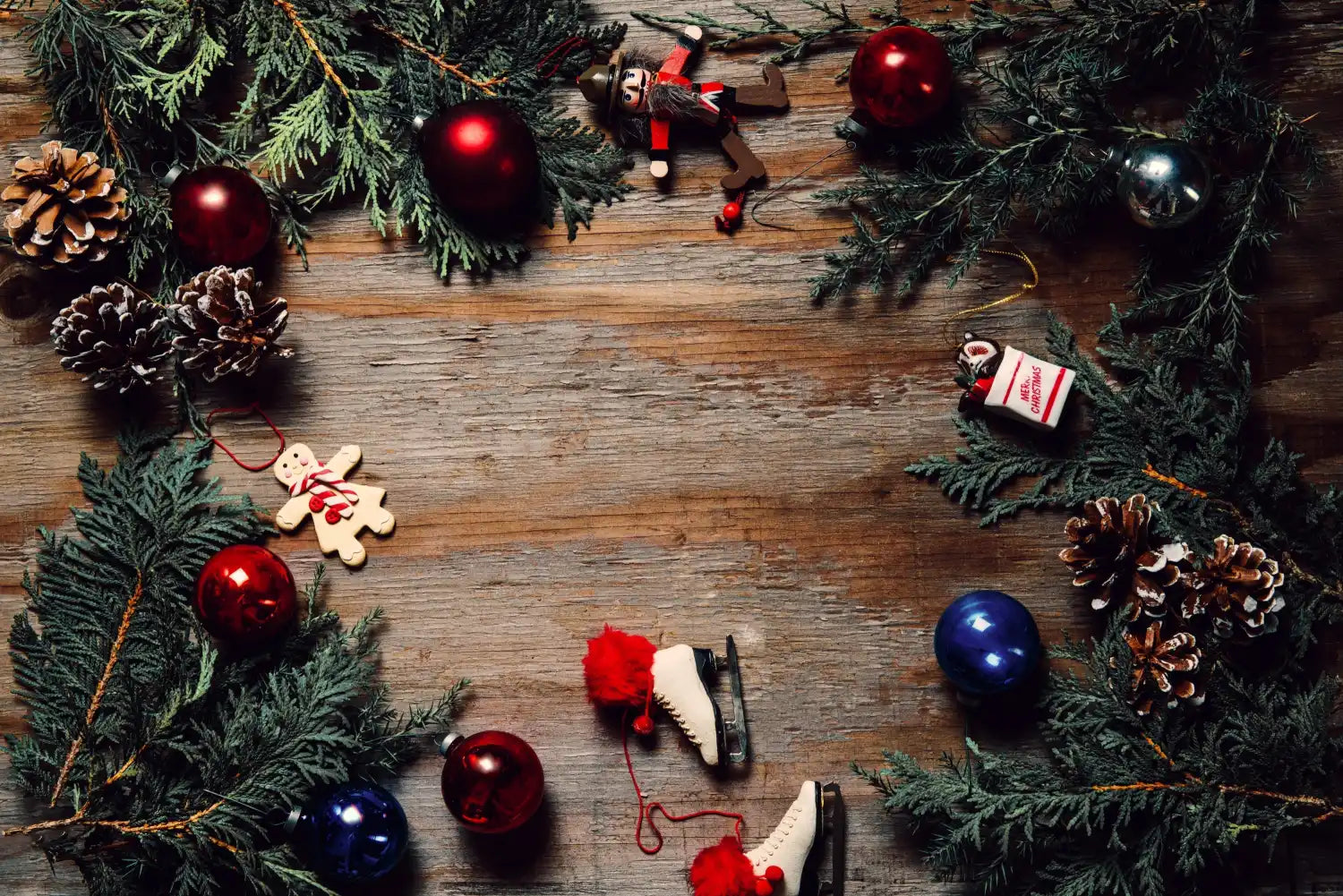 Christmas wreath decorated with red and blue ornaments, pinecones, and evergreen branches on wooden planks.