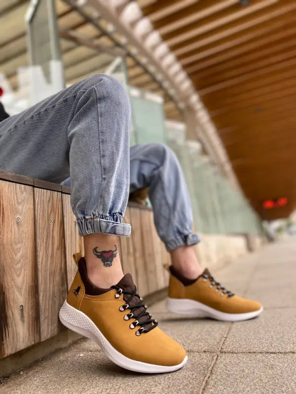 Tan leather sneakers with white soles and dark laces paired with rolled-up gray jeans.