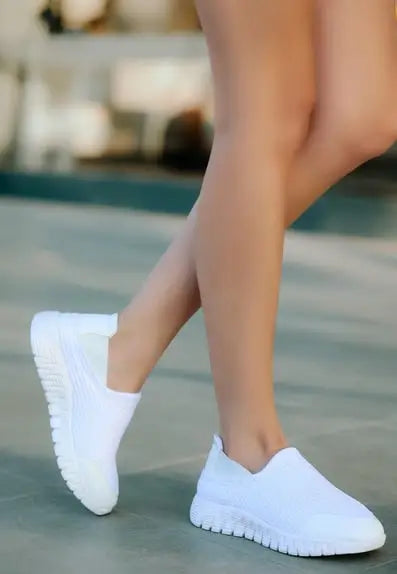 Pair of white slip-on athletic sneakers with a knit mesh upper and flexible sole.