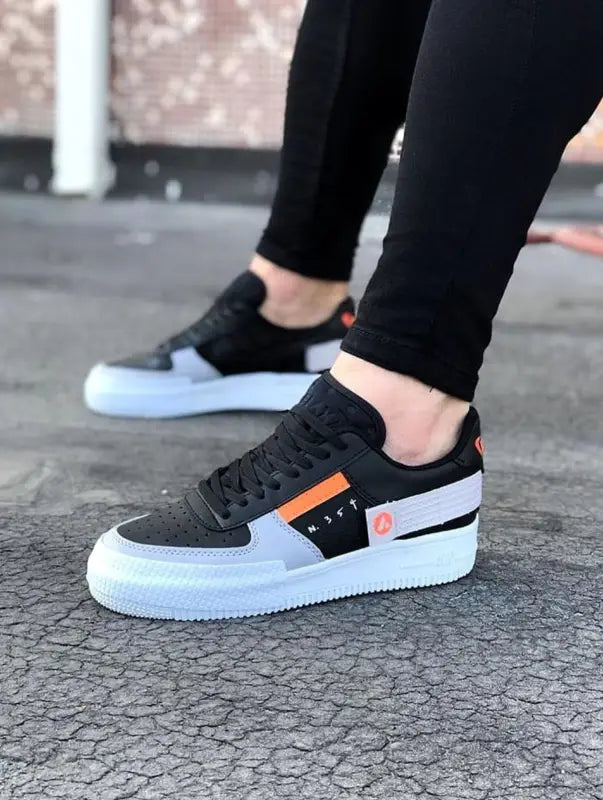 Black and white sneaker with an orange accent stripe on the side.