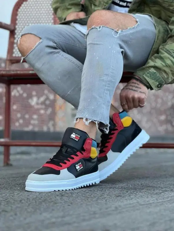 Black and red sneakers with white soles and colorful accents worn with ripped jeans.