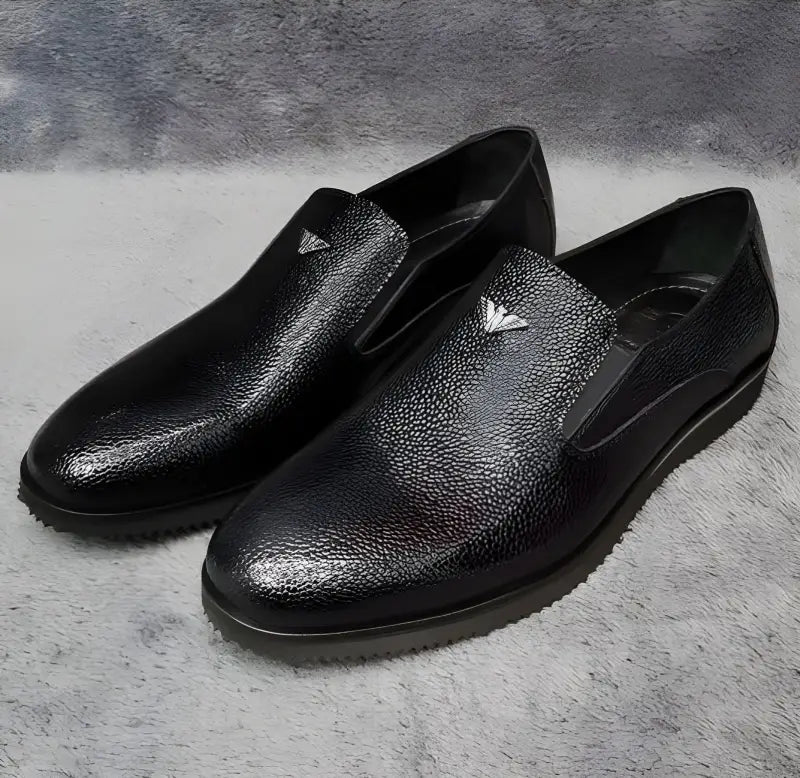 Black leather slip-on dress shoes with textured uppers and flat soles.