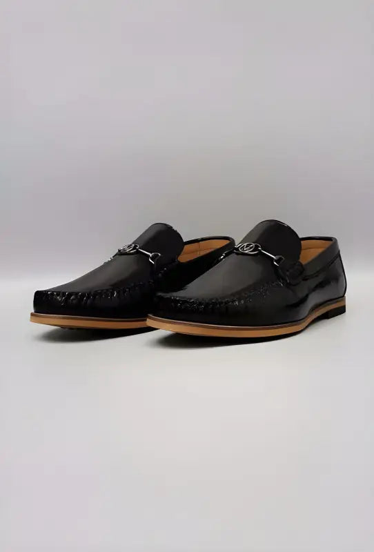 Black leather loafers with silver buckle details and tan soles.