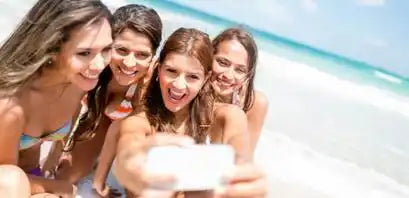 A group of friends laughing while looking at something together on a beach.