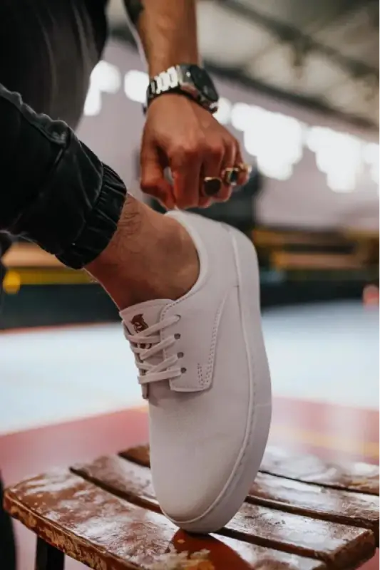 Clean white sneaker with laces being adjusted by a hand wearing a watch.