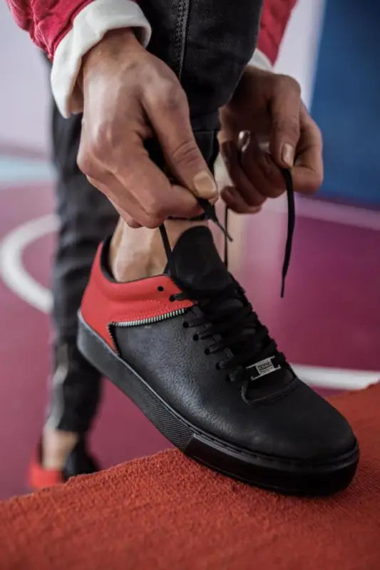 Black and red leather sneaker being laced up.