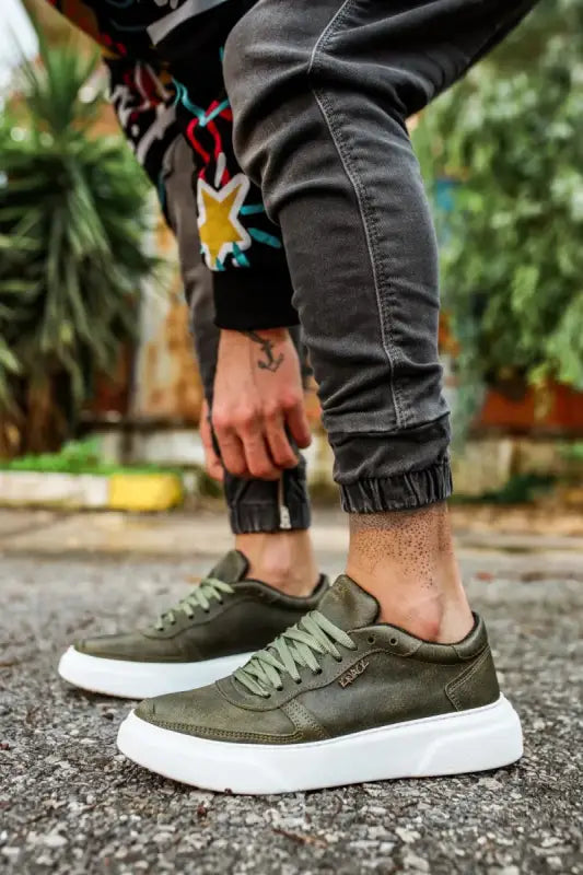 Olive green sneakers with white platform soles and black jogger pants.