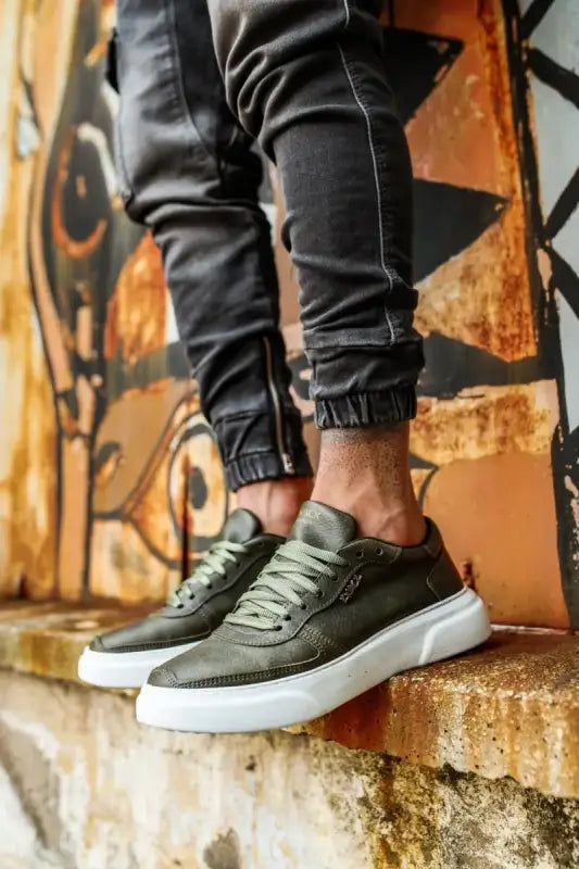 Olive green sneakers with white soles and black jogger pants.