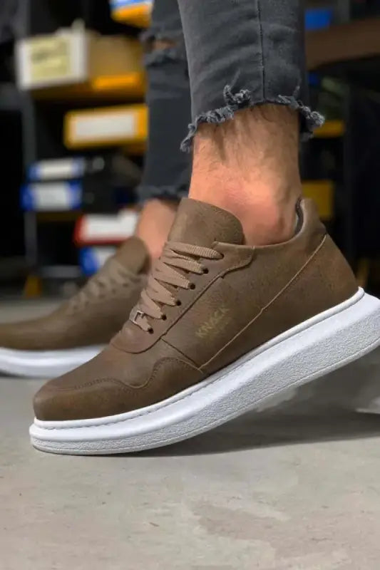 Brown leather sneaker with white sole and distressed denim visible above.