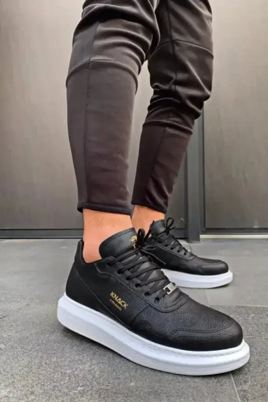 Black sneakers with white soles and gold accents worn with dark pants.