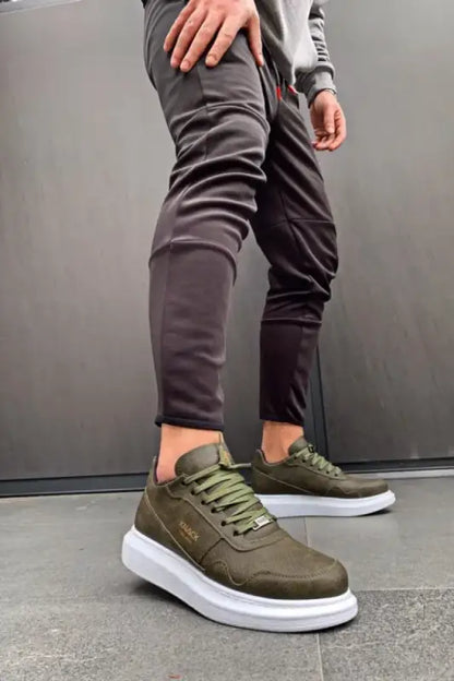 Olive green sneakers with white soles and matching laces worn with gray pants.