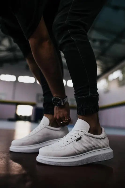 White perforated leather sneakers with a thick sole and black rolled-up pants above them.