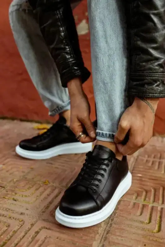 Black leather sneakers with white soles and laces being tied.