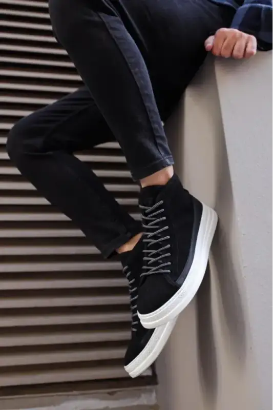 Black high-top sneaker with white sole and laces worn with dark pants.