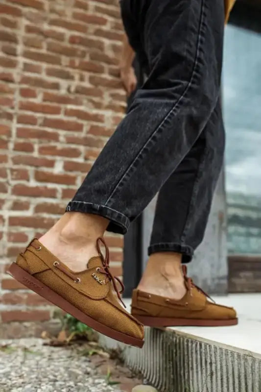 Brown leather boat shoes with laces worn with dark jeans.