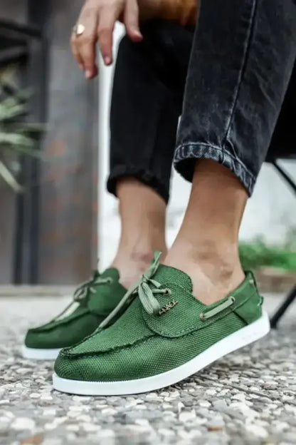 Green leather boat shoes with white soles and decorative tassels.