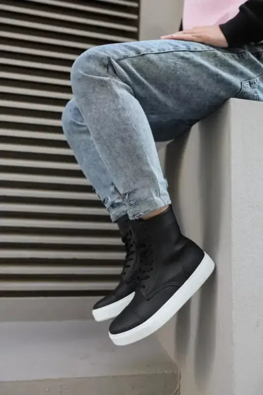 Black high-top sneaker with white sole worn with distressed blue jeans.