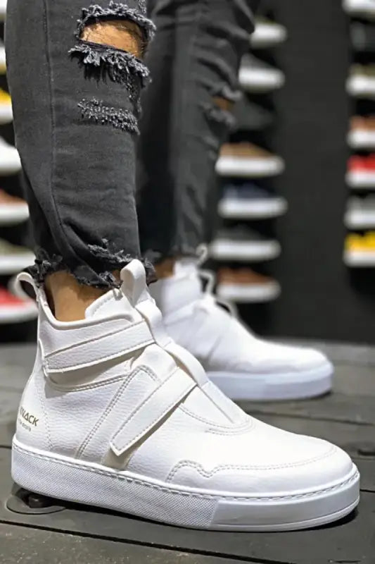 White high-top sneakers with velcro straps worn with ripped black jeans.