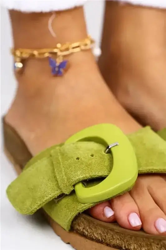 Lime green suede sandal with a buckle detail and white-painted toenails visible.