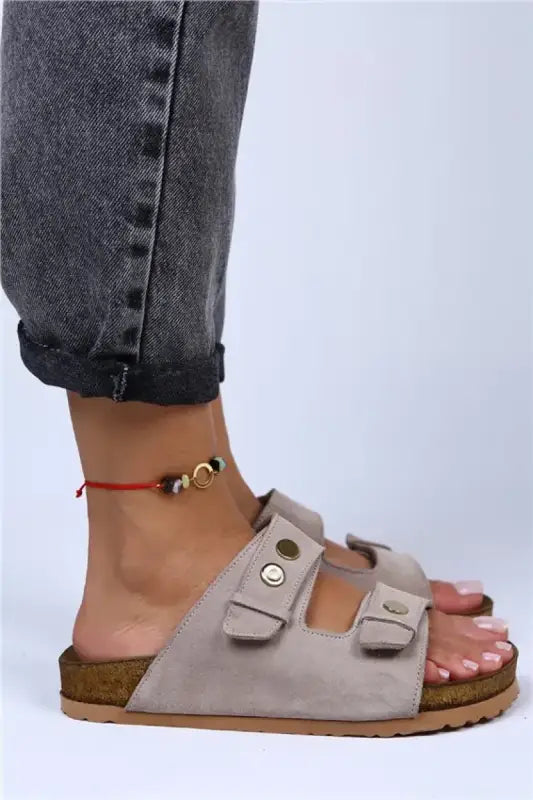 Beige suede Birkenstock-style sandal with two buckle straps worn with a red ankle bracelet.