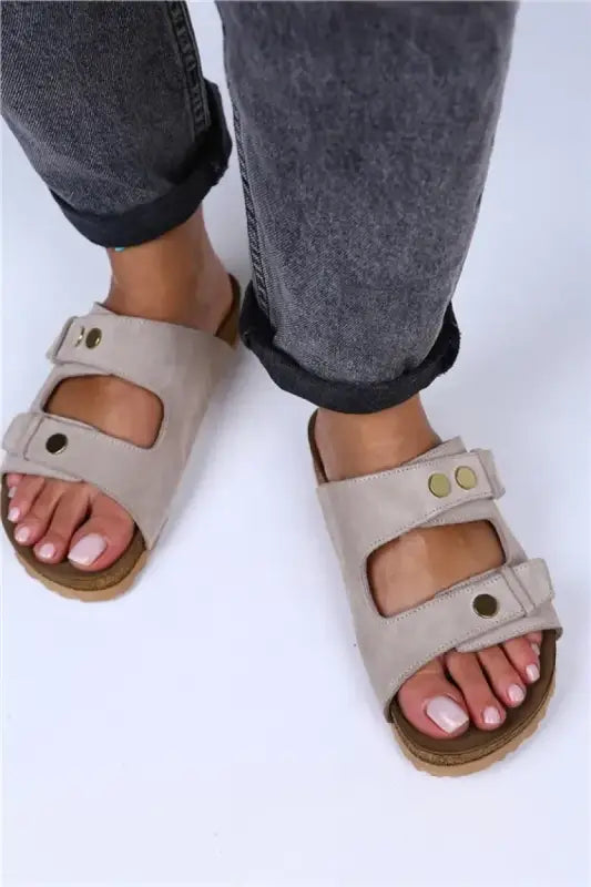 Beige double-strap Birkenstock-style sandals with metal buckles and a cork footbed.