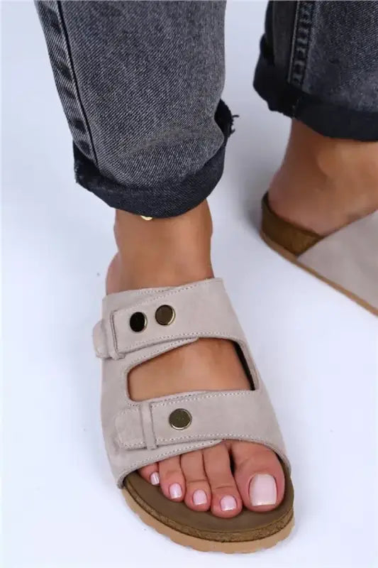 Beige double-strap sandal with metal snaps worn with rolled-up jeans.