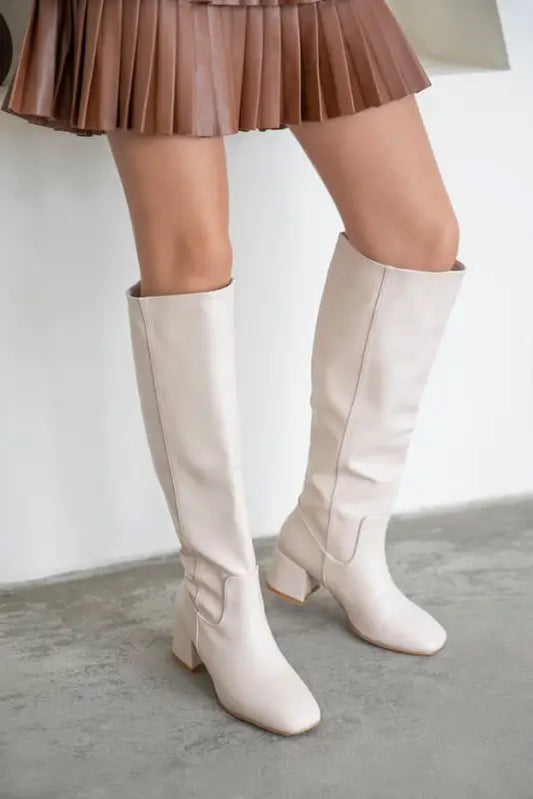 Pair of cream-colored knee-high boots with square toes and low block heels.