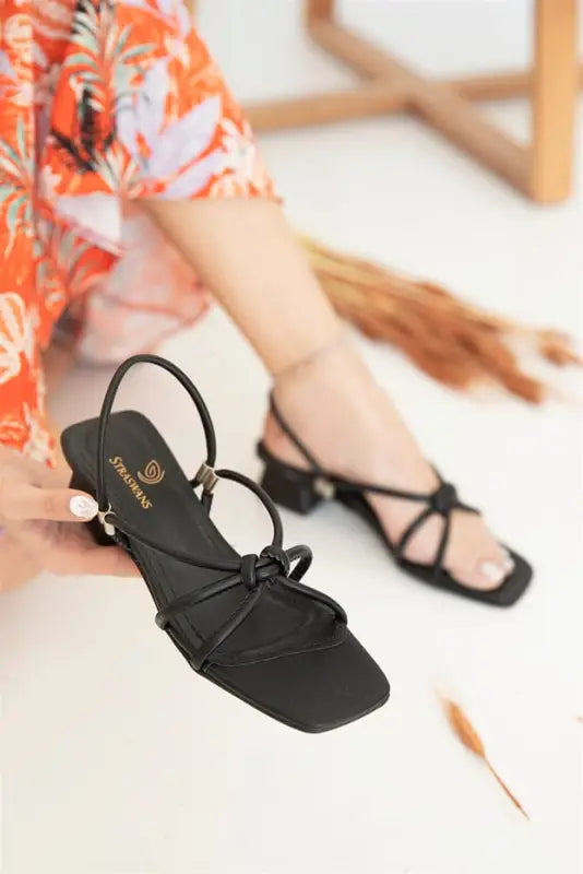 Black strappy sandals with delicate bow details and thin heels.