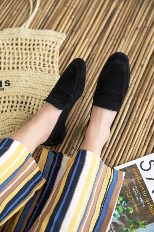 Black suede loafers worn with striped pants.