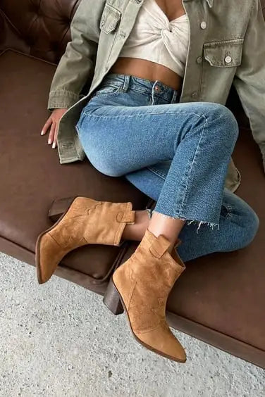 Tan suede ankle boots with a chunky heel paired with cropped blue jeans and a khaki jacket.